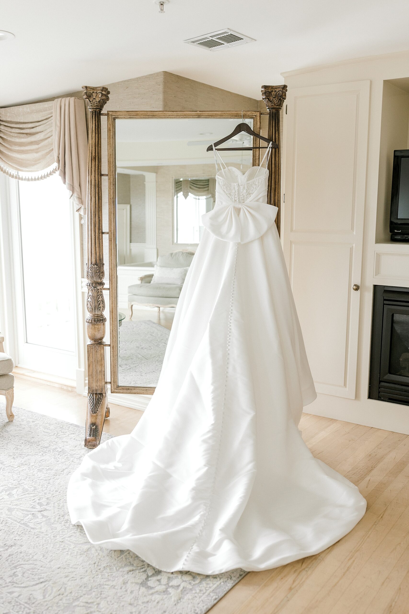 wedding dress with bow hangs on gold framed mirror inside suite at Bonnet Island Estate