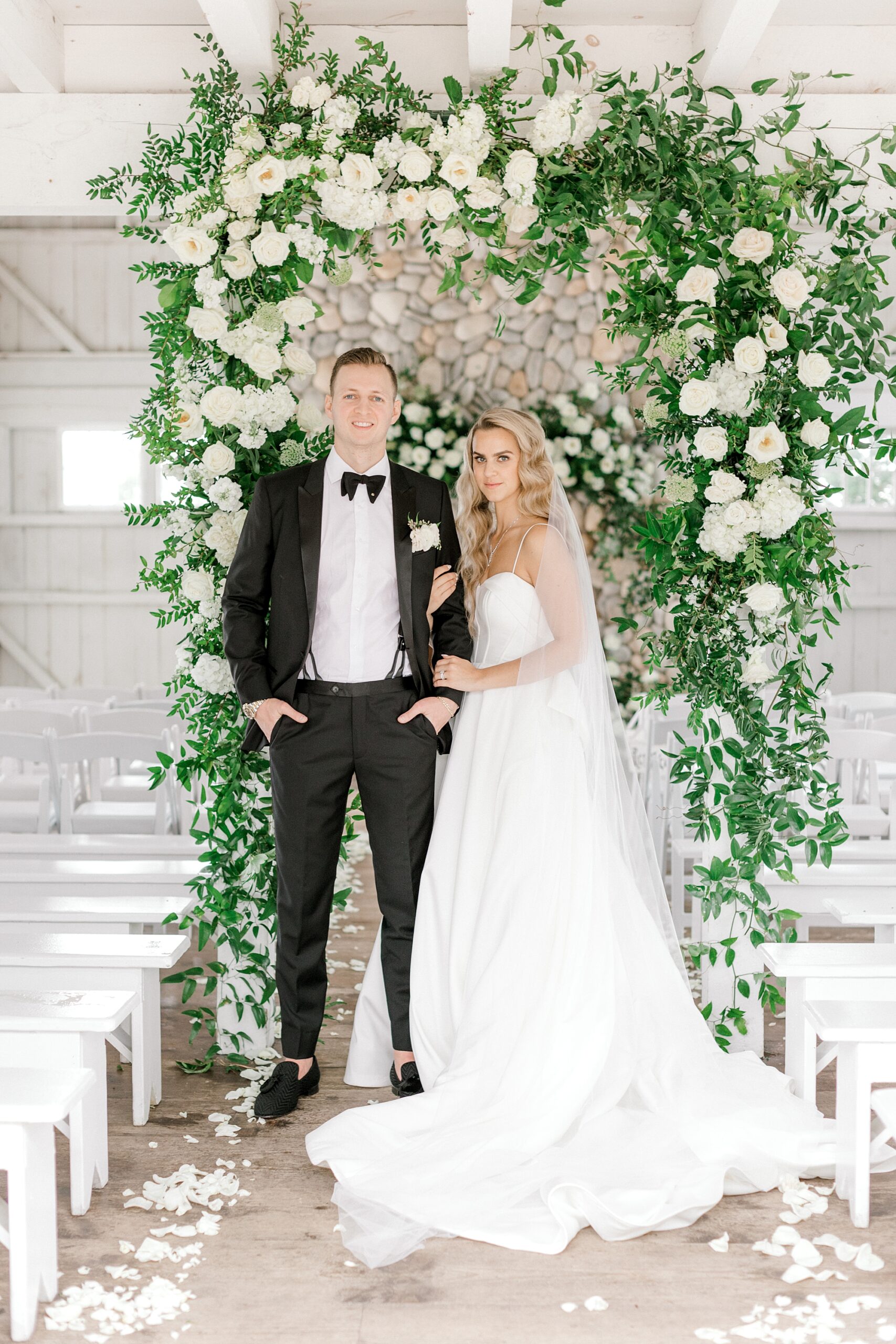 bride and groom pose in front of arbor with white flowers and greenery inside Bonnet Island Estate