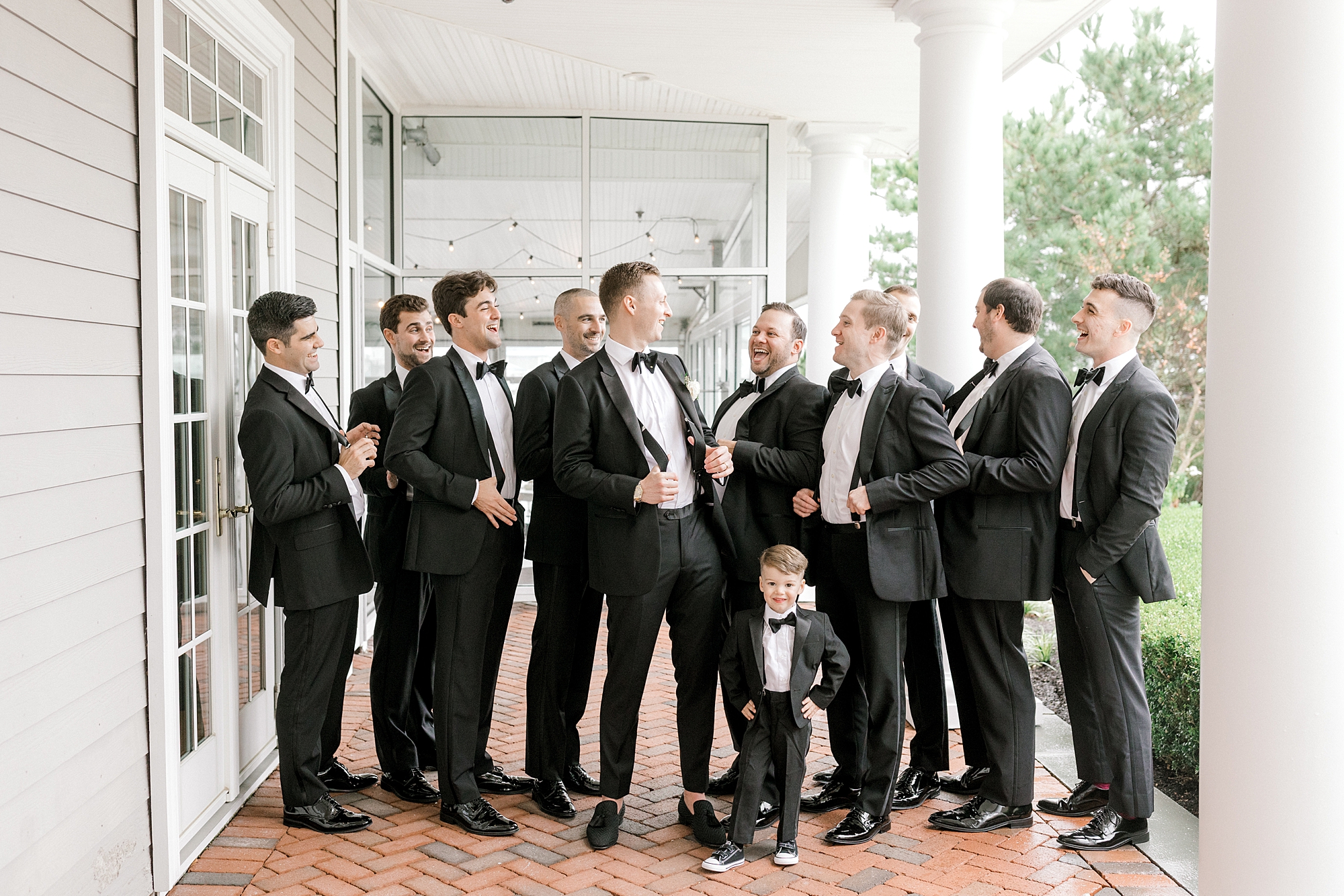 groom and groomsmen in black suits laugh under awning at Bonnet Island Estate