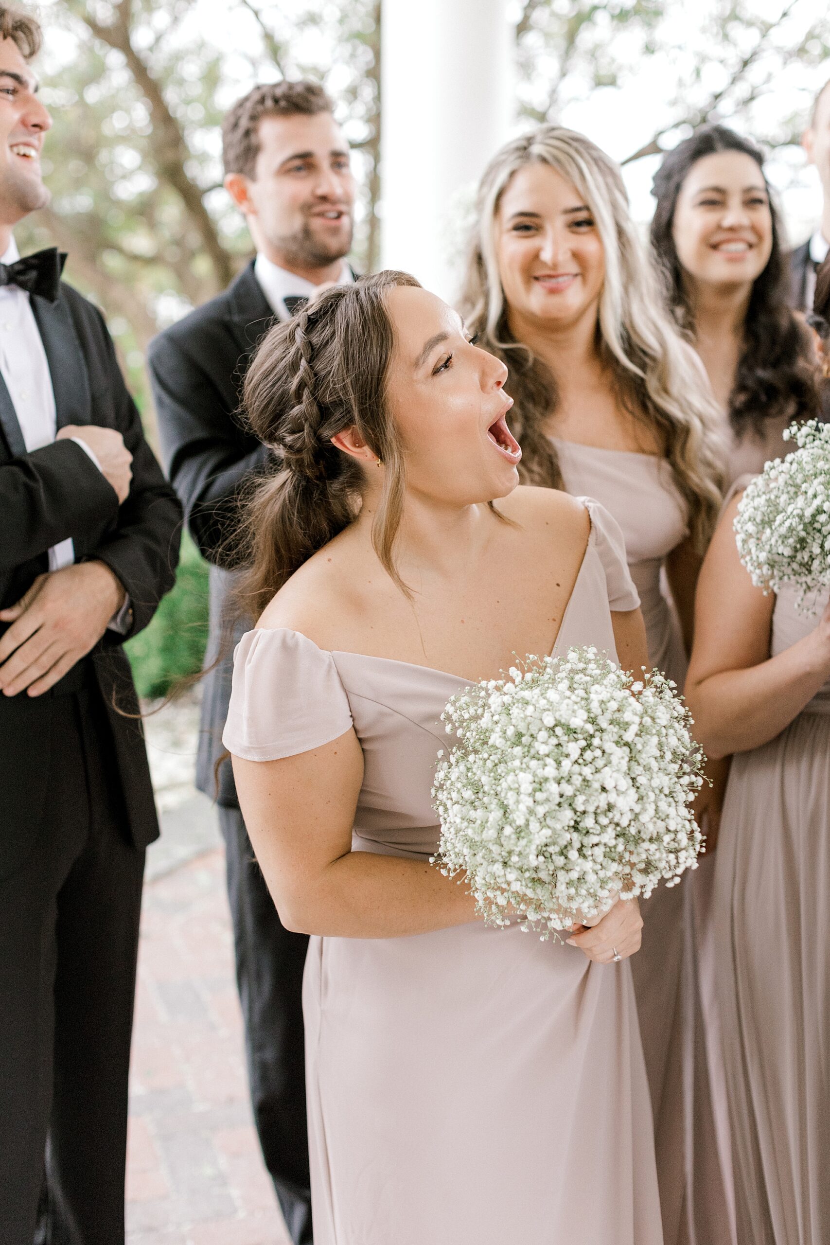 bride holding bouquet of baby's breath makes face towards newlyweds