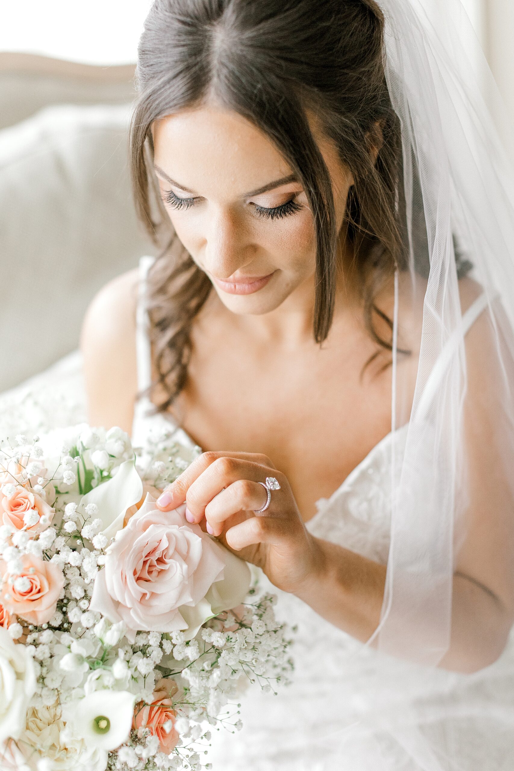 bride reaches to touch leaves of roses in her bouquet of peach and white flowers