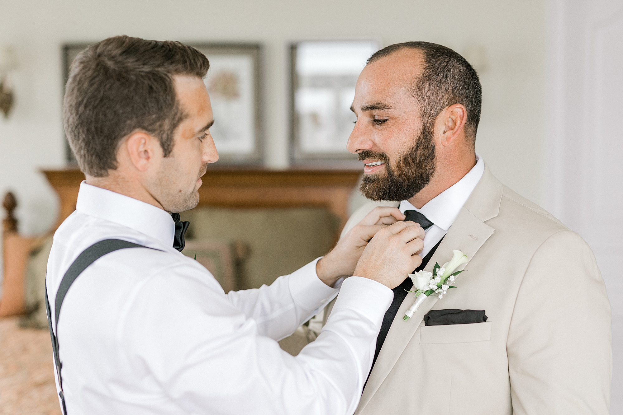 groomsman adjusts tie for groom in tan suit before Bonnet Island Estate wedding