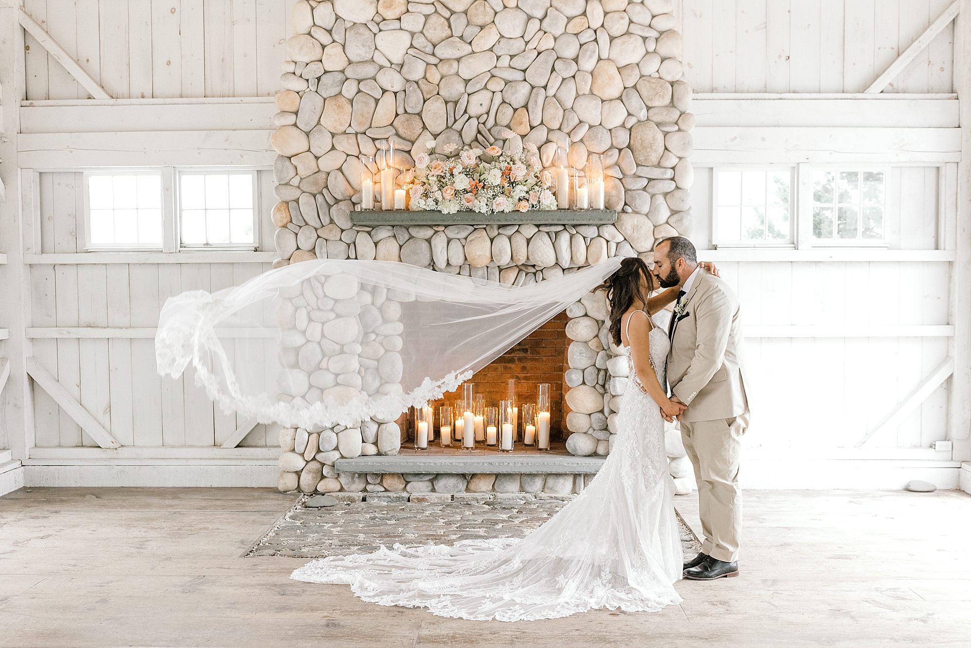 bride and groom hug in front of stone fireplace with veil floating behind them