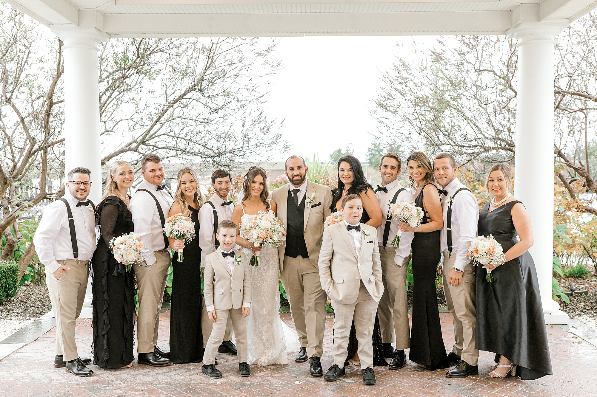 bride and groom stand with wedding party in tan and black a