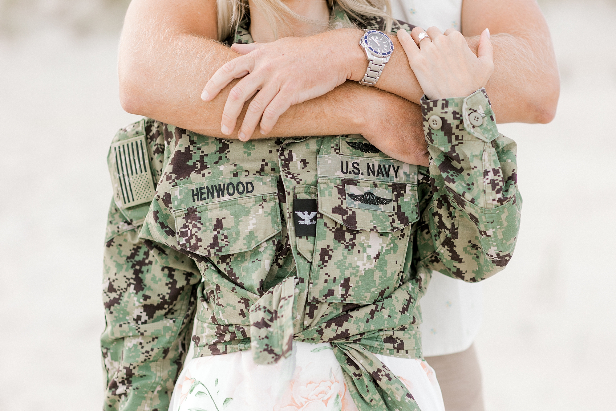 woman wearing Army jacket is hugged by man from behind during Long Beach Island engagement session on Brant Beach