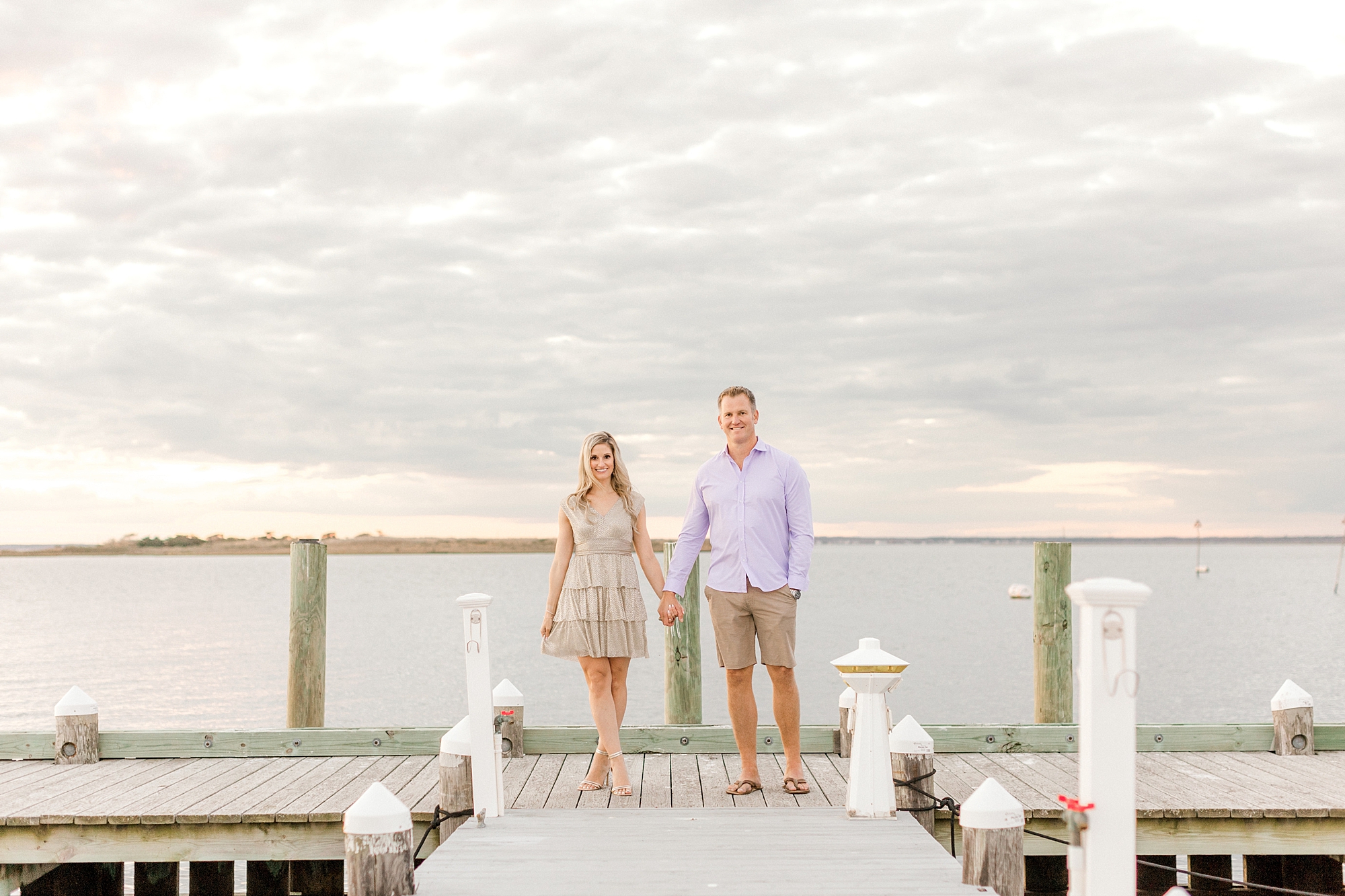 man and woman walk on dock holding hands during summer Long Beach Island engagement session