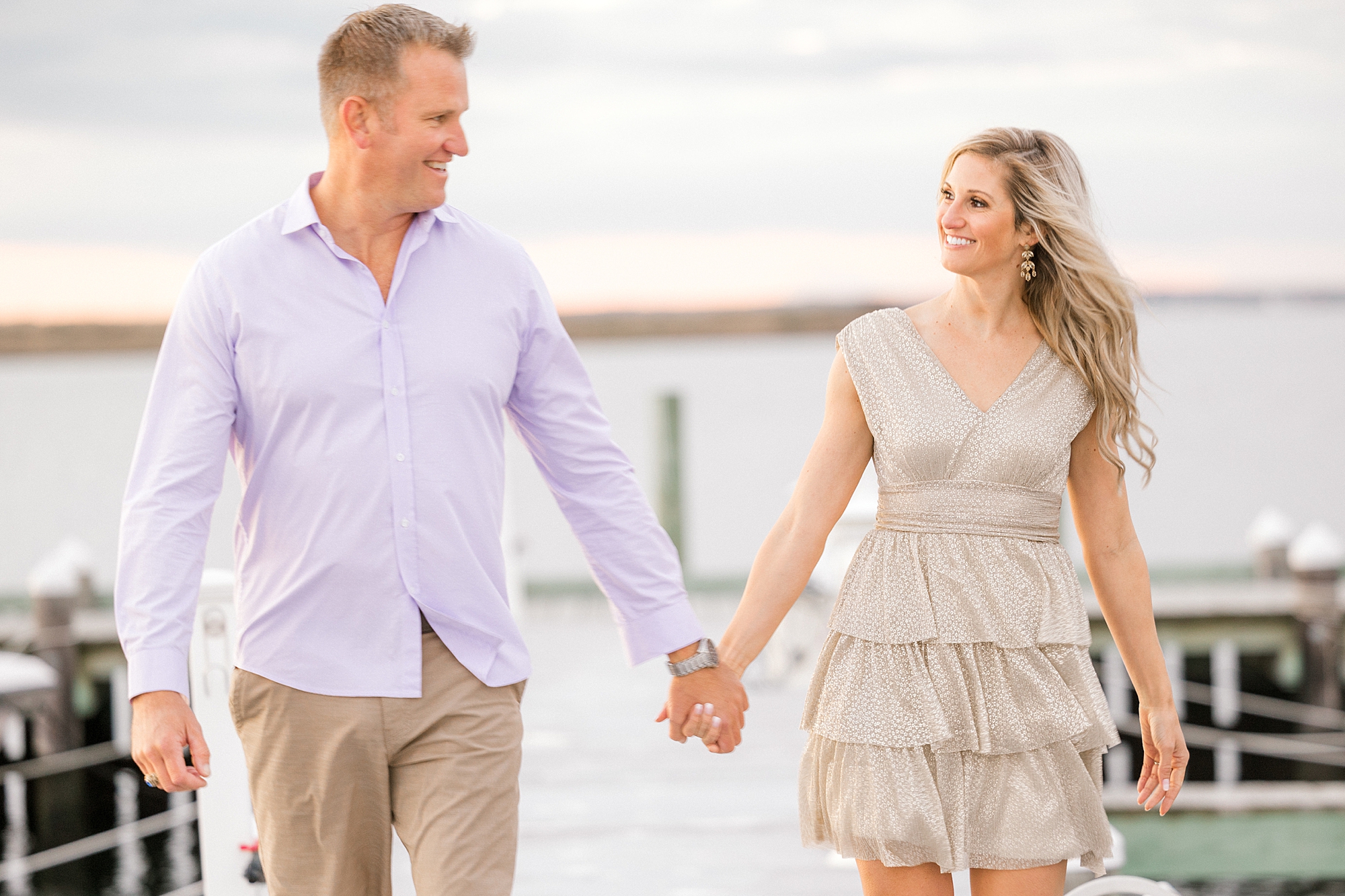 man and woman hold hands walking on pier during Long Beach Island engagement session at Brant Beach
