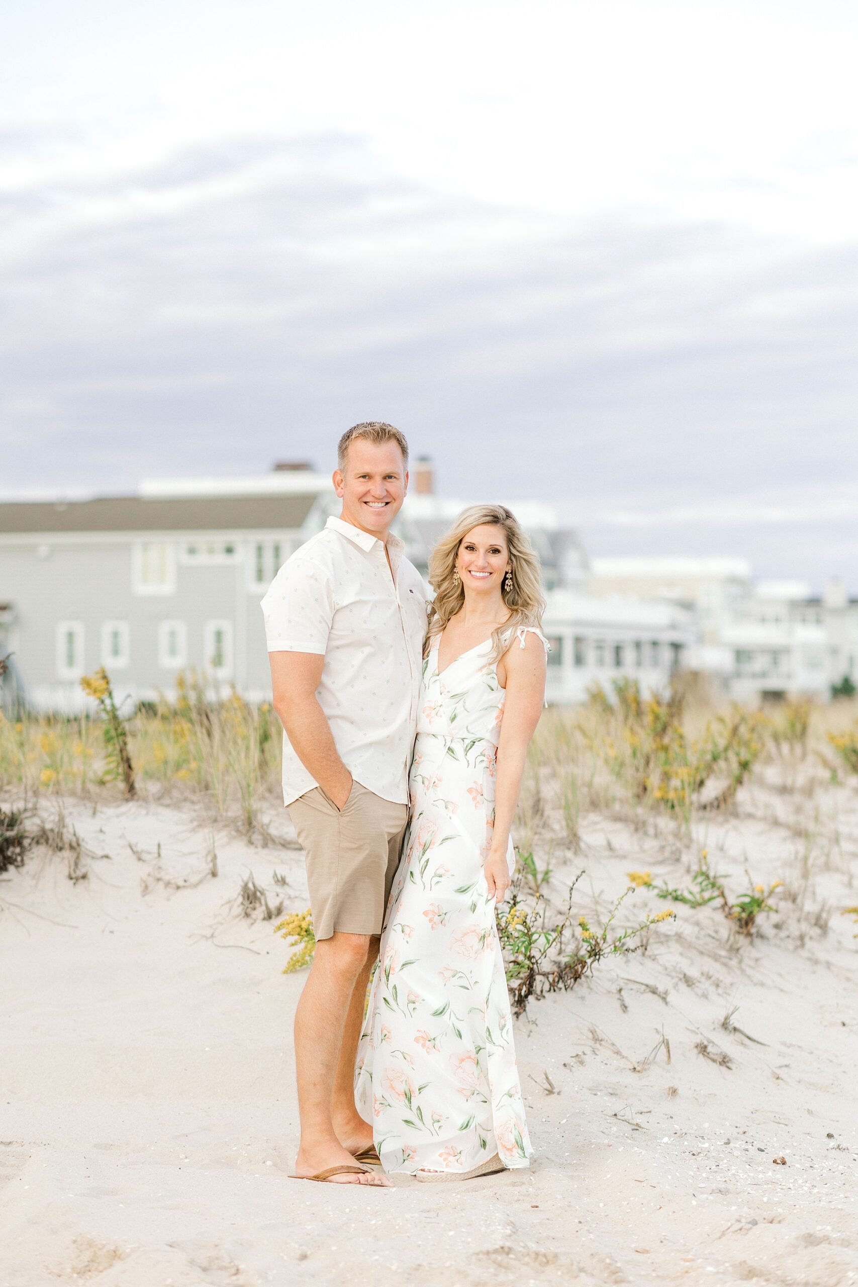engaged couple stands in front of sand dunes during Long Beach Island engagement session on Brant Beach