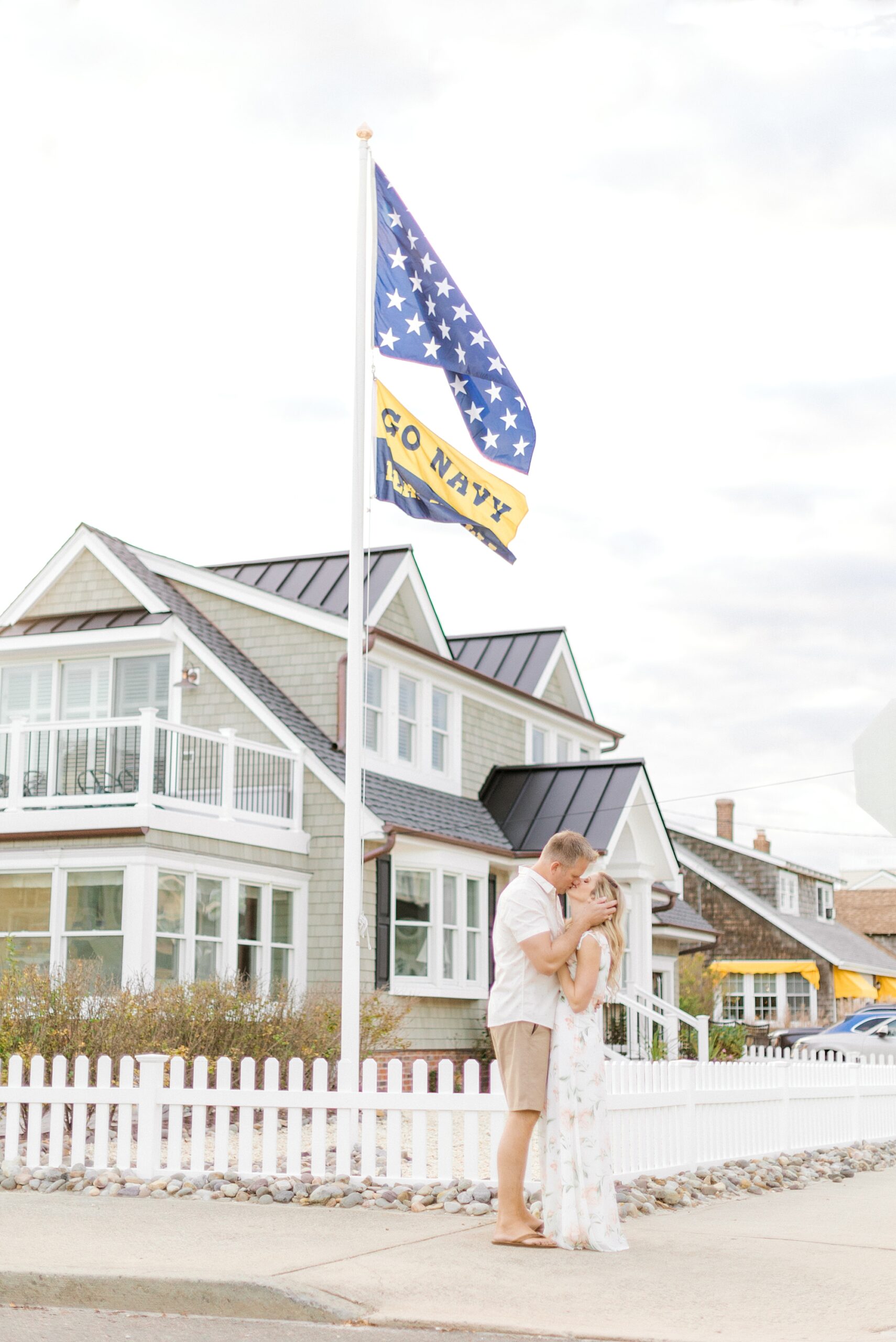 engaged couple kisses near white picket fence at Brant Beach