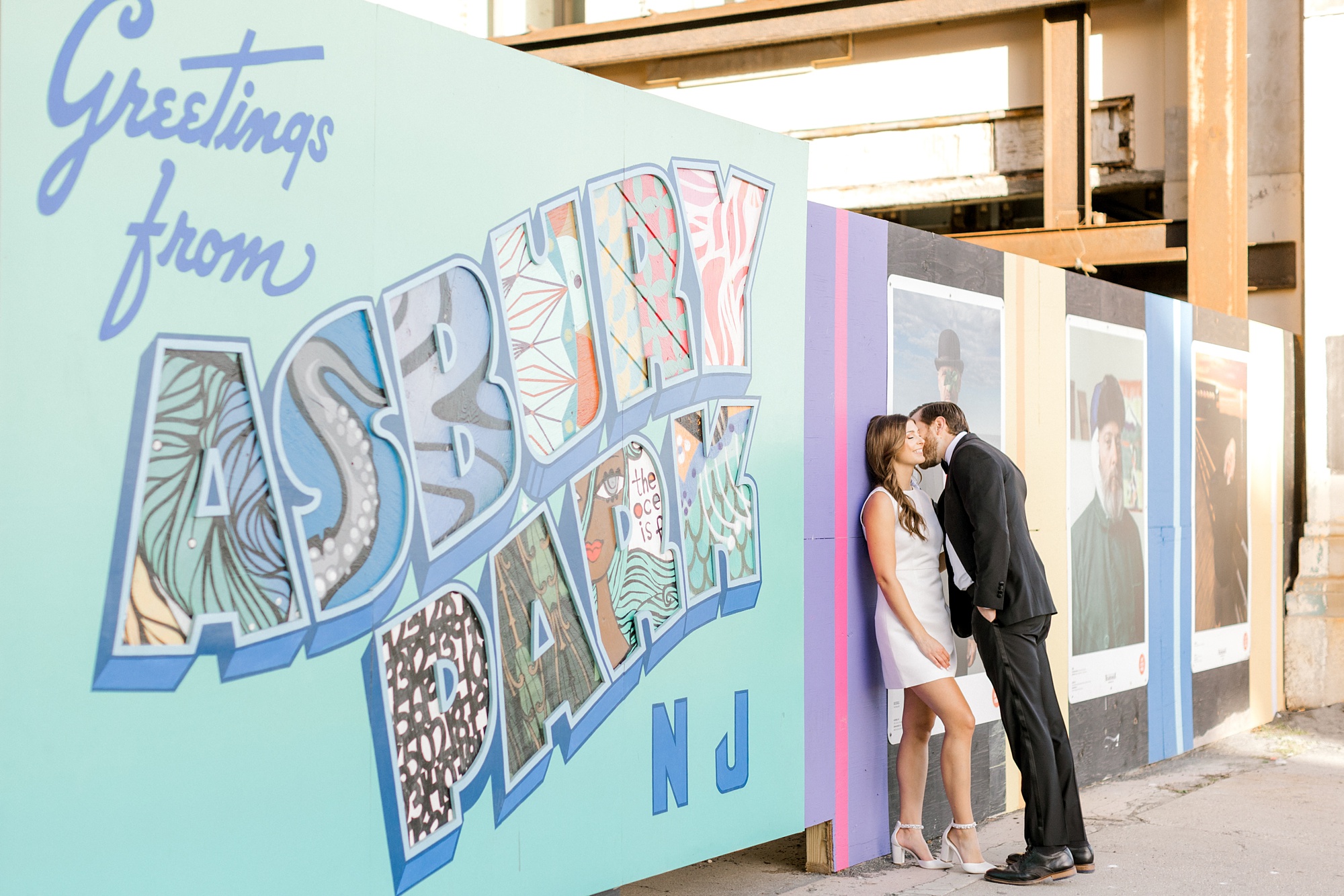 man leans to kiss woman against colorful signs at Asbury Park