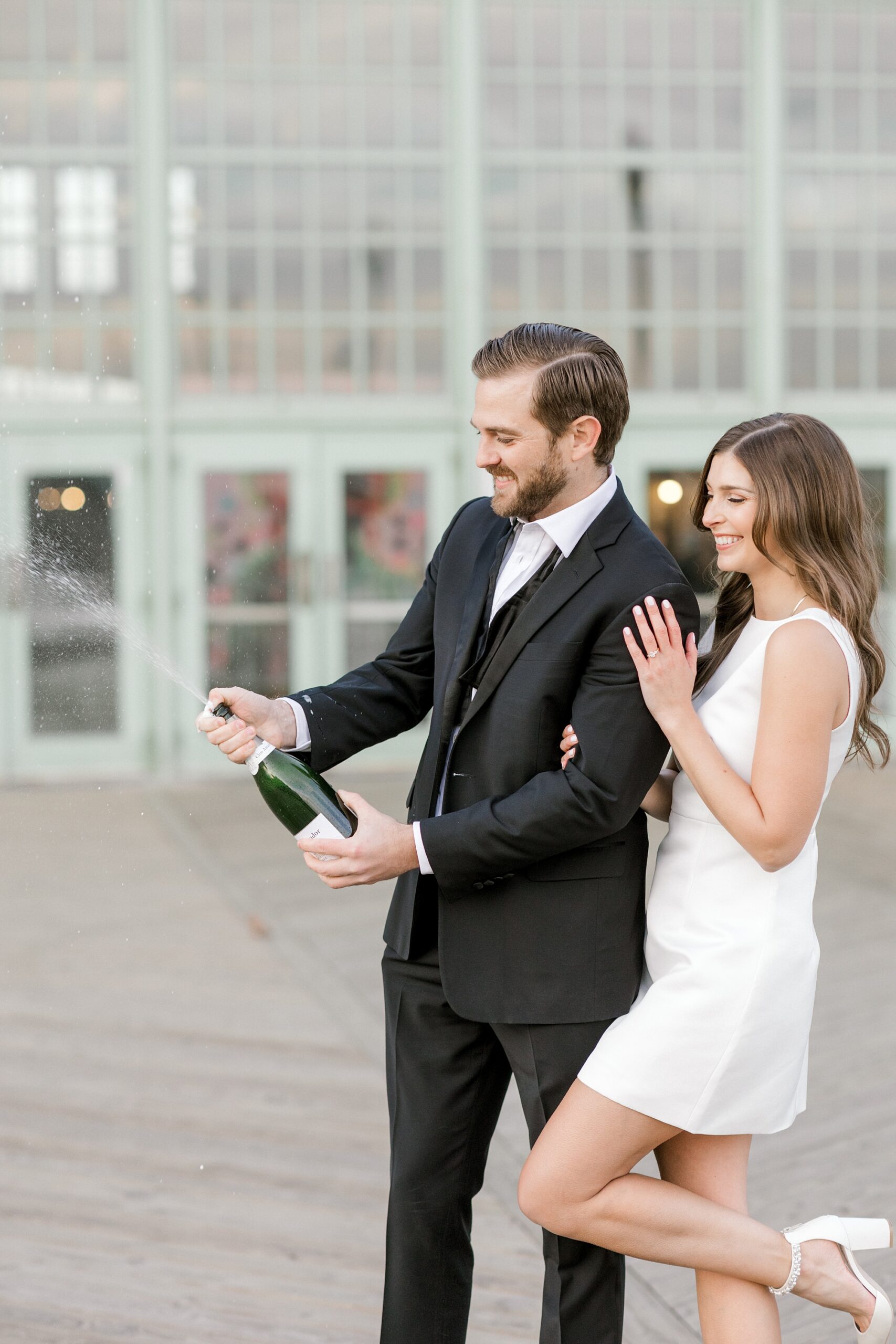 couple pops champagne during engagement portraits on boardwalk in Asbury Park NJ