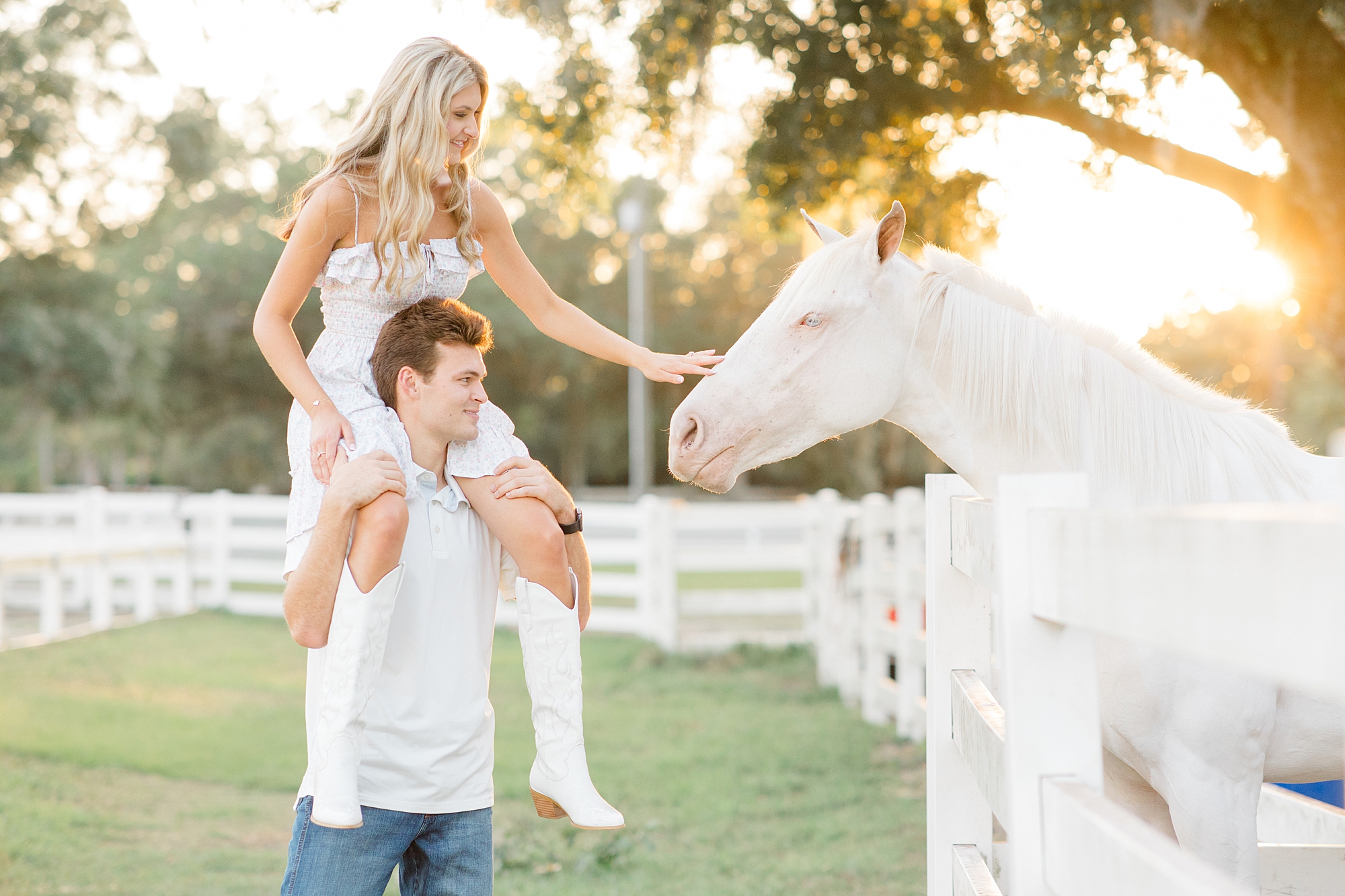 man puts fiancee on his shoulders to pet white horse at Distinctive Stables