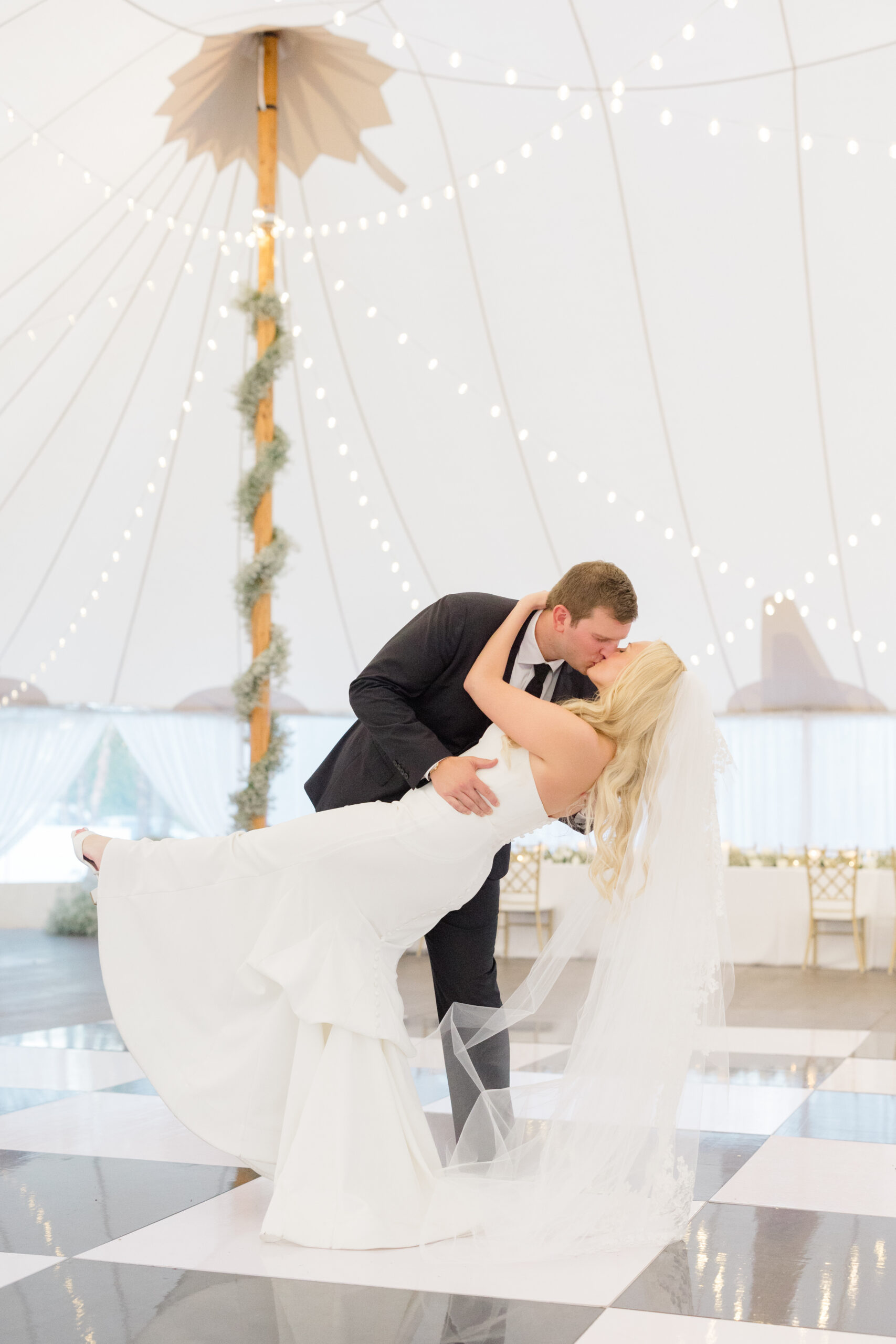 Groom dipping a bride on a black and white checkered dance floor in a tented wedding reception
