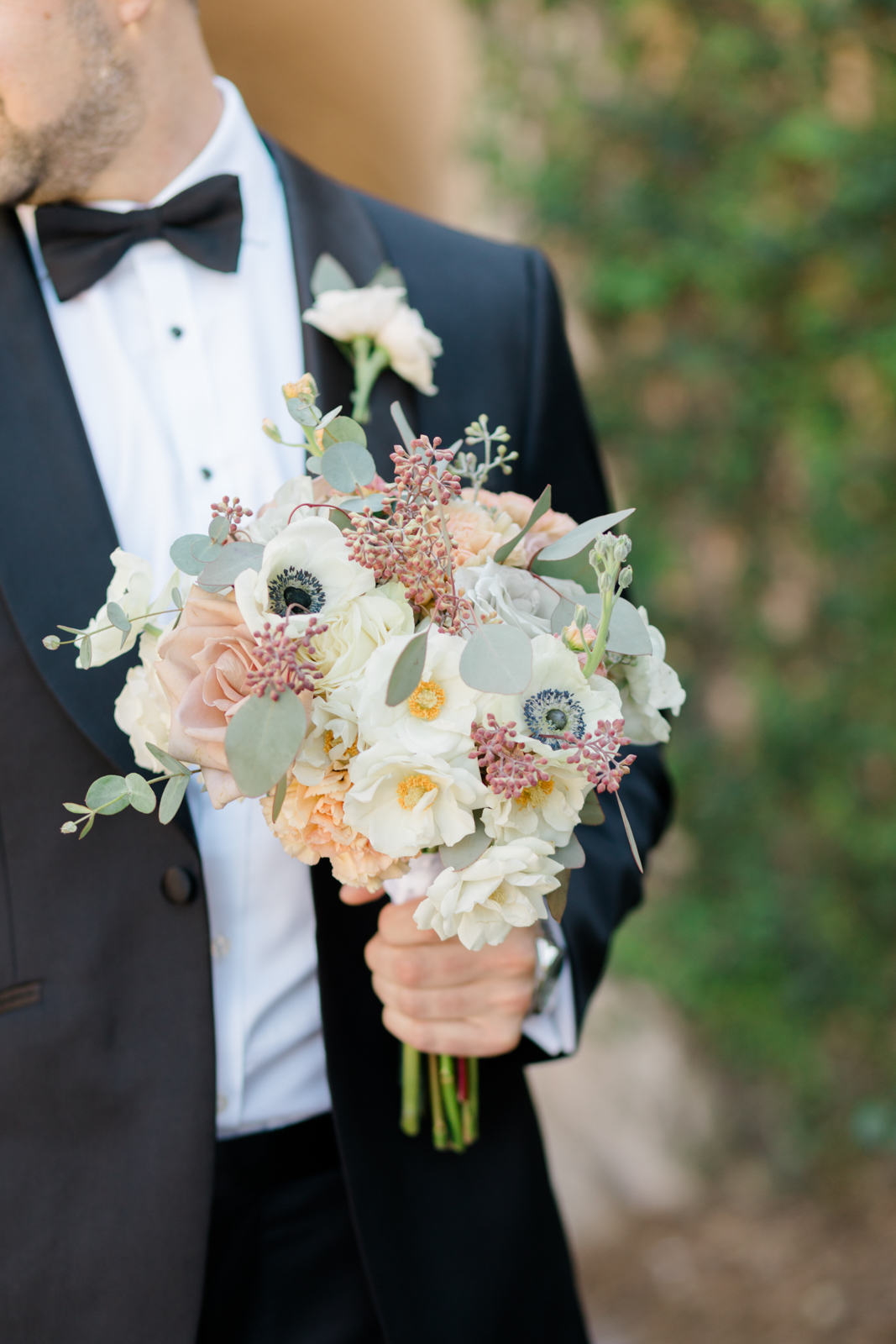 Groom holds bridal bouquet while wearing tuxedo