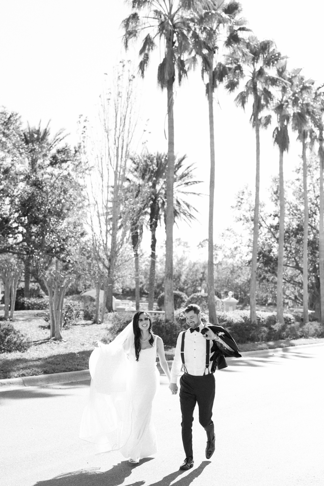 black and white photo if a bride and groom running down a palm tree lined street