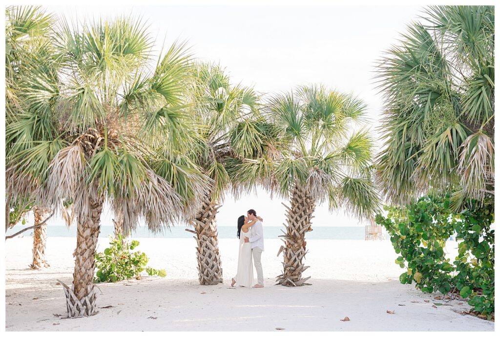 a couple kissing under 2 palm trees at Lido Key beach