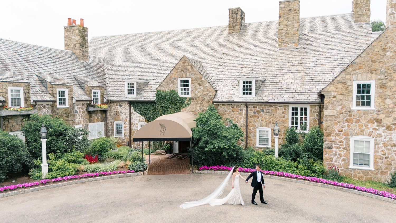 Abby and Will photographed from above by drone in front of the stone clubhouse at Fiddler's Elbow Country Club, NJ wedding photographer Susan Elizabeth Photography